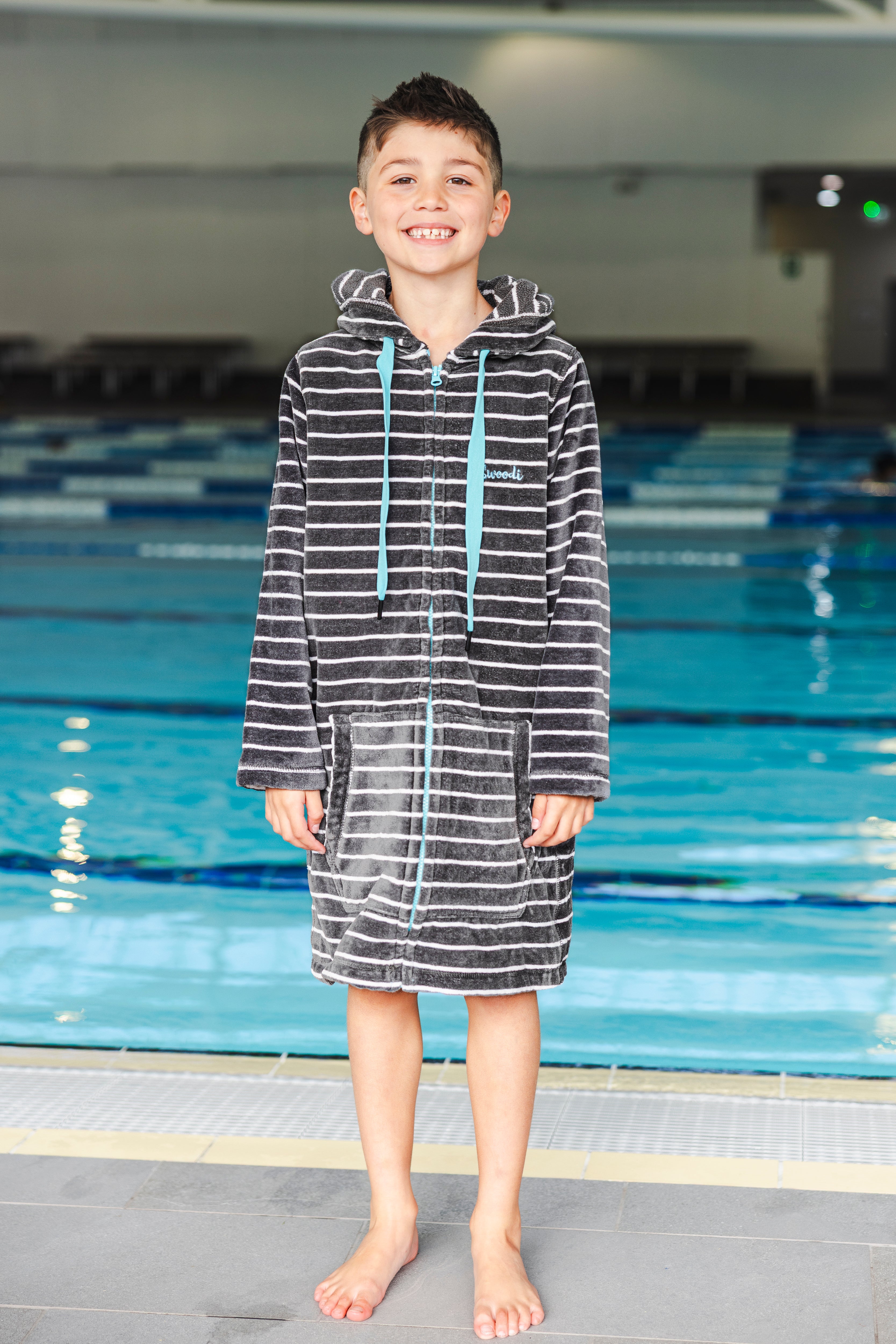Child wearing a striped hooded towel by a pool