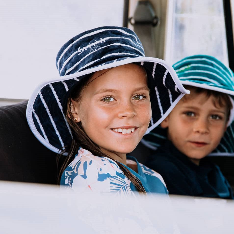 Young girl sitting in car at the beach wearing swimwear and Swoodi sun protection hat with UPF 50+