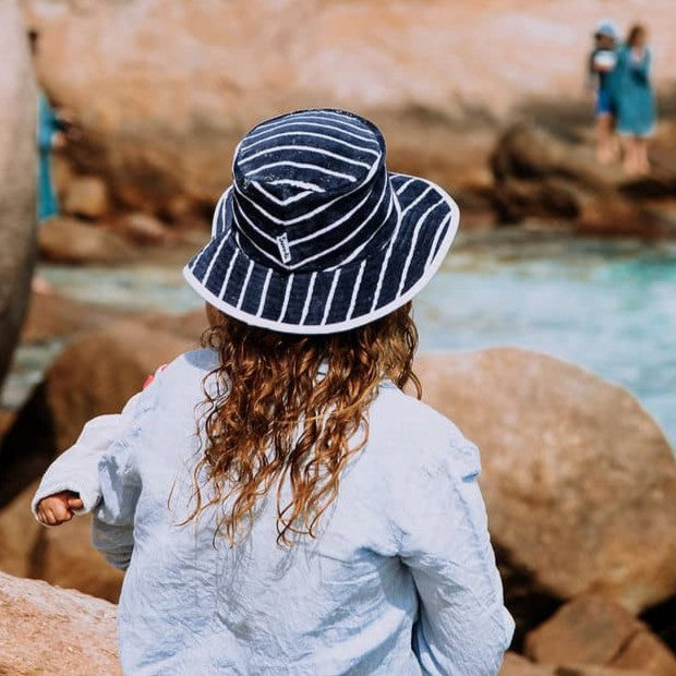 Back view of a mum holding her baby at the beach wearing Swoodi toweling bucket hat with UPF 50+ sun protection