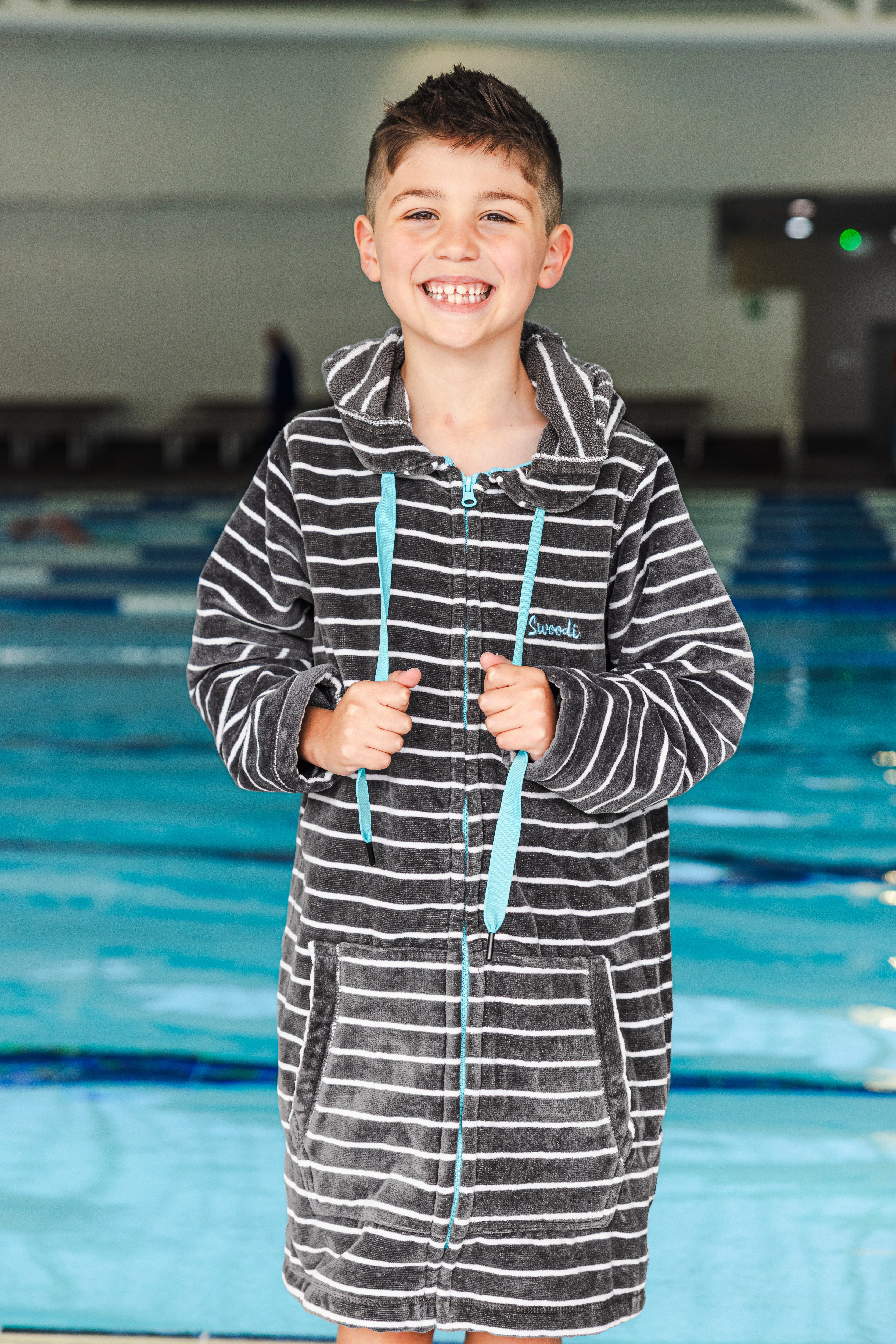 Child wearing a towelling striped robe in an indoor pool setting