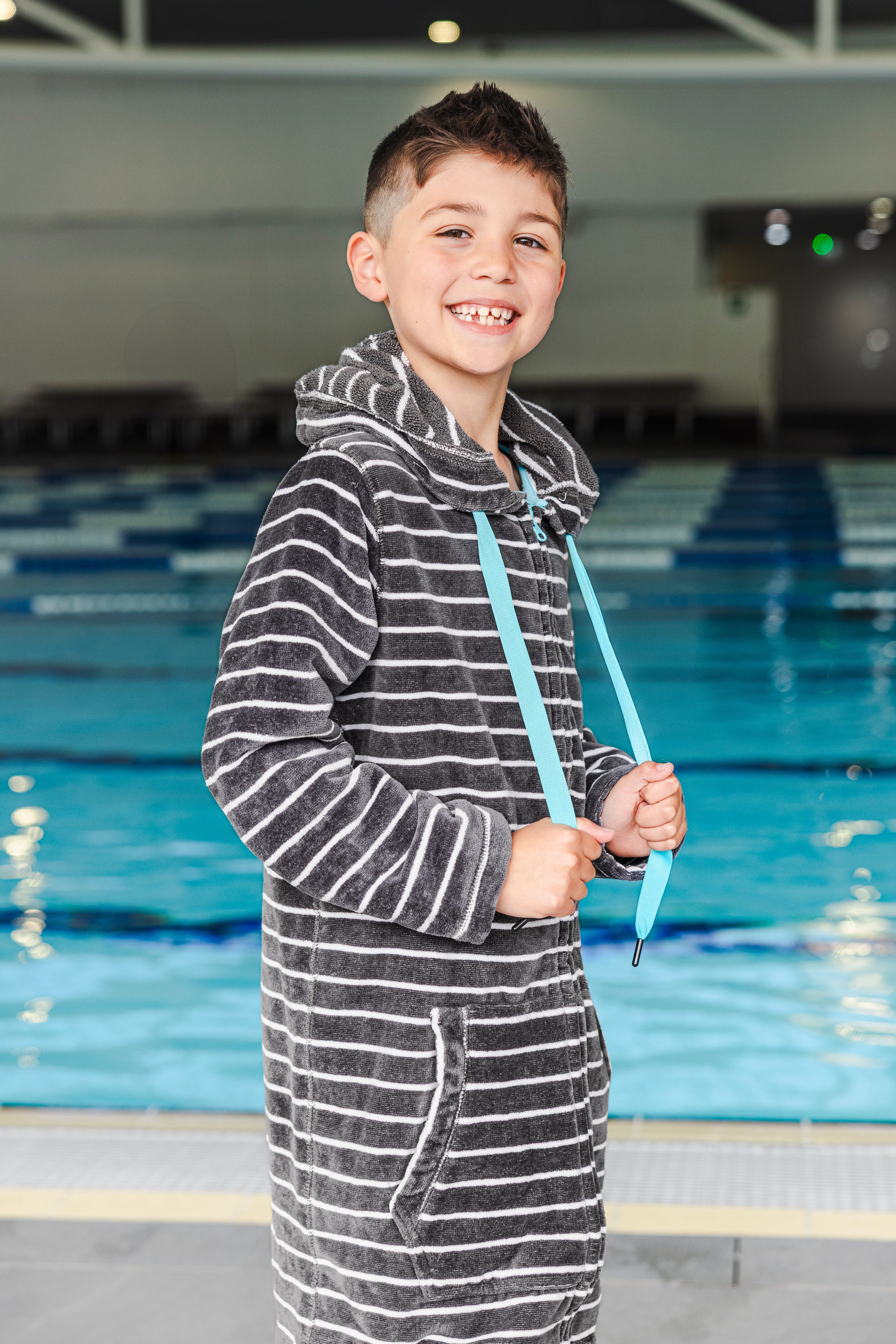 Child wearing a striped zip up towel holding a blue ribbon by a pool