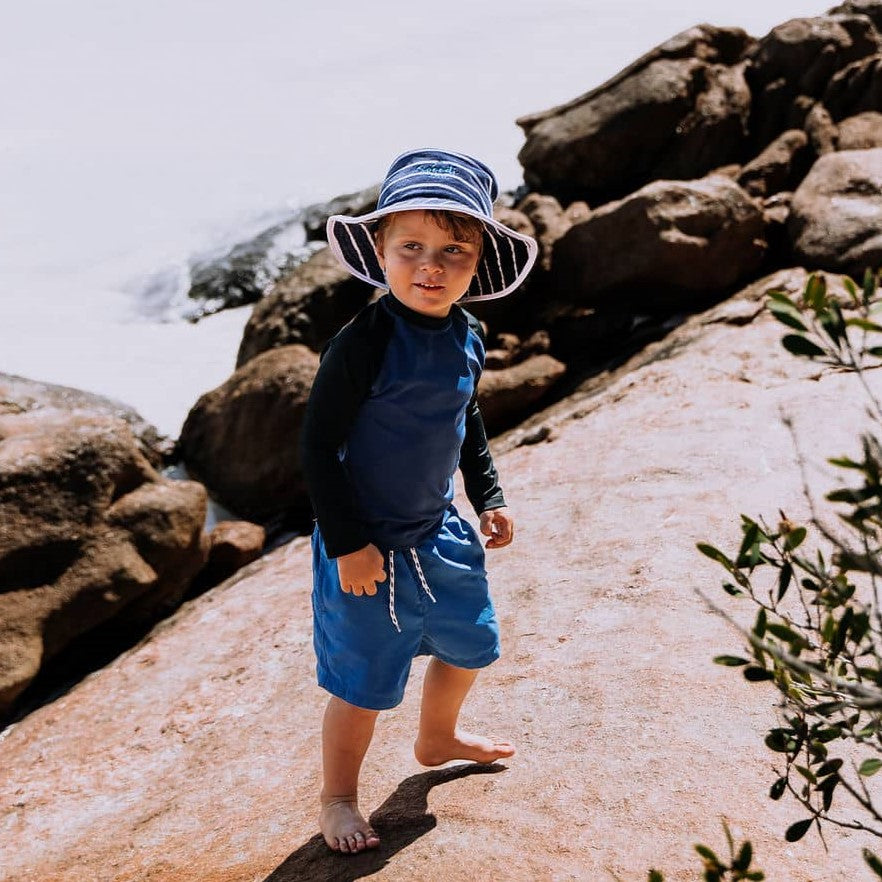 Boy wearing swimwear and Swoodi wide brimmed sun protection hat, while exploring on the rocks at Esperance beach. 