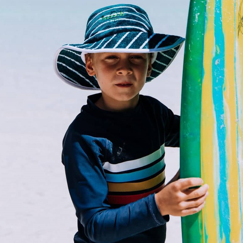 Boy at Esperance beach holding surf board wearing a Swoodi toweling bucket hat, UPF 50 +