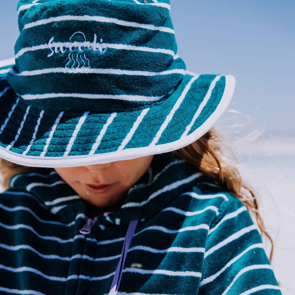 Young girl at the beach wearing Swoodi UPF 50+ toweling bucket hat in turquoise with matching zip up beach robe