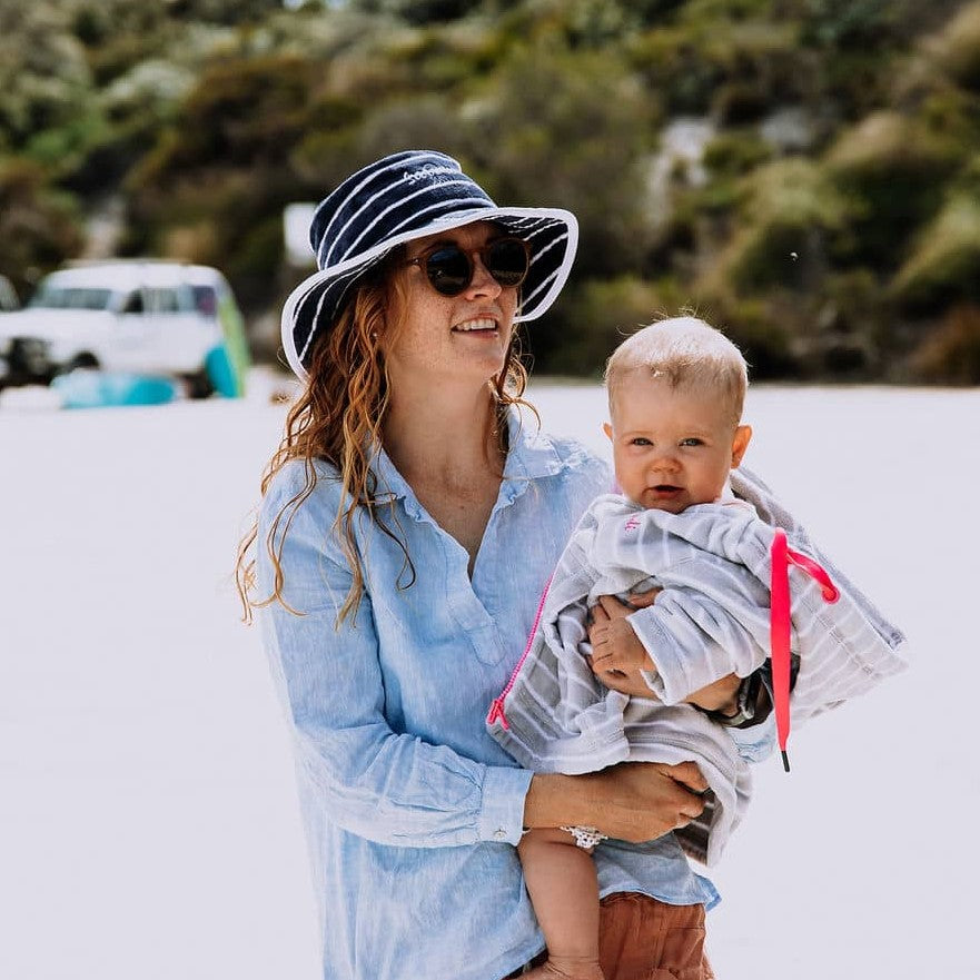 a Mum wearing Swoodi Bucket hat at the beach, while carrying her baby wearing swoodi swim robe 