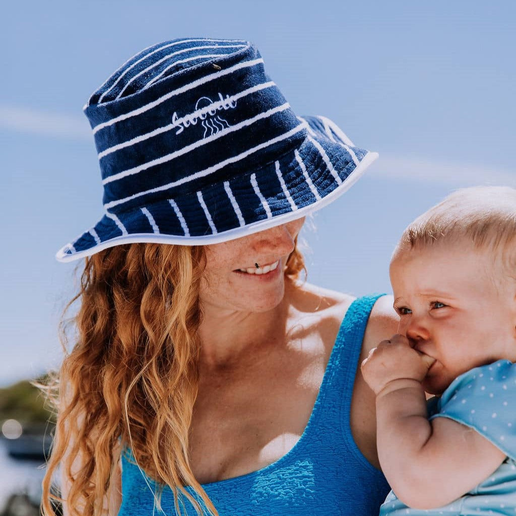 Close up of a Mum holding her baby wearing swimwear and Swoodi toweling bucket hat in navy and white stripe  